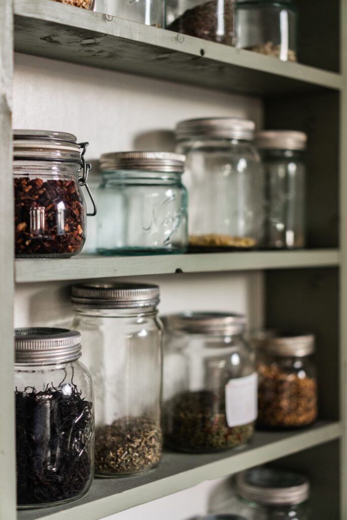 Dried herbs in glass jars on a shelf. 