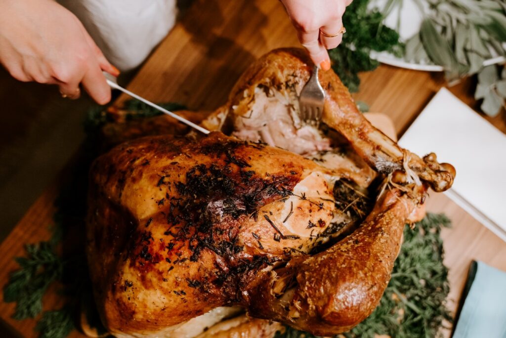 A person carving a roast turkey that is covered in herbs.