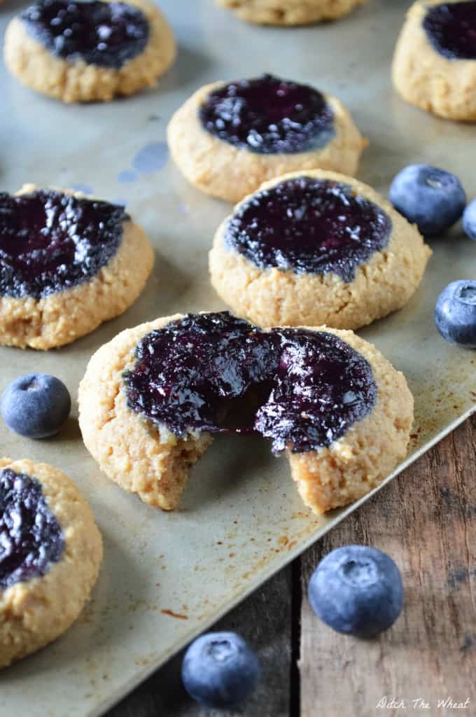 Almond flour thumbprint cookies with a blueberry filling on a cookie sheet with blueberries.