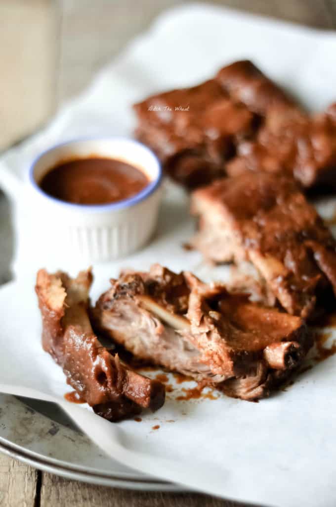 Slow cooker ribs in a cooking sheet with parchment paper and a bowl of bbq sauce.