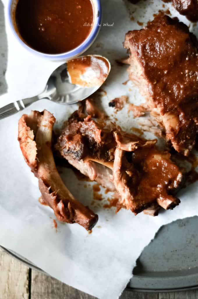 Slow cooker ribs in a cooking sheet with parchment paper and a bowl of bbq sauce.