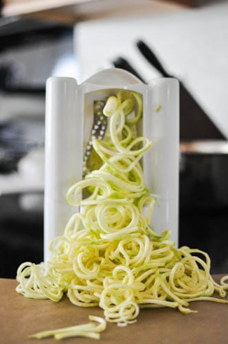 Zucchini noodles coming out of a spiralizer. 