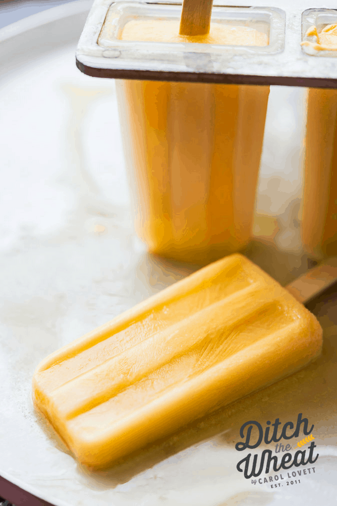 Healthy orange creamsicle popsicles in the popsicle mold with one popsicle out.