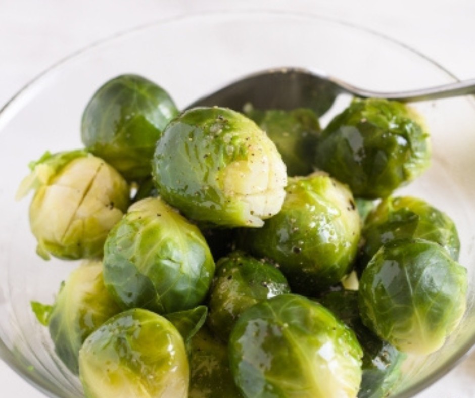 A glass bowl filled with cooked Brussels sprouts with a spoon.
