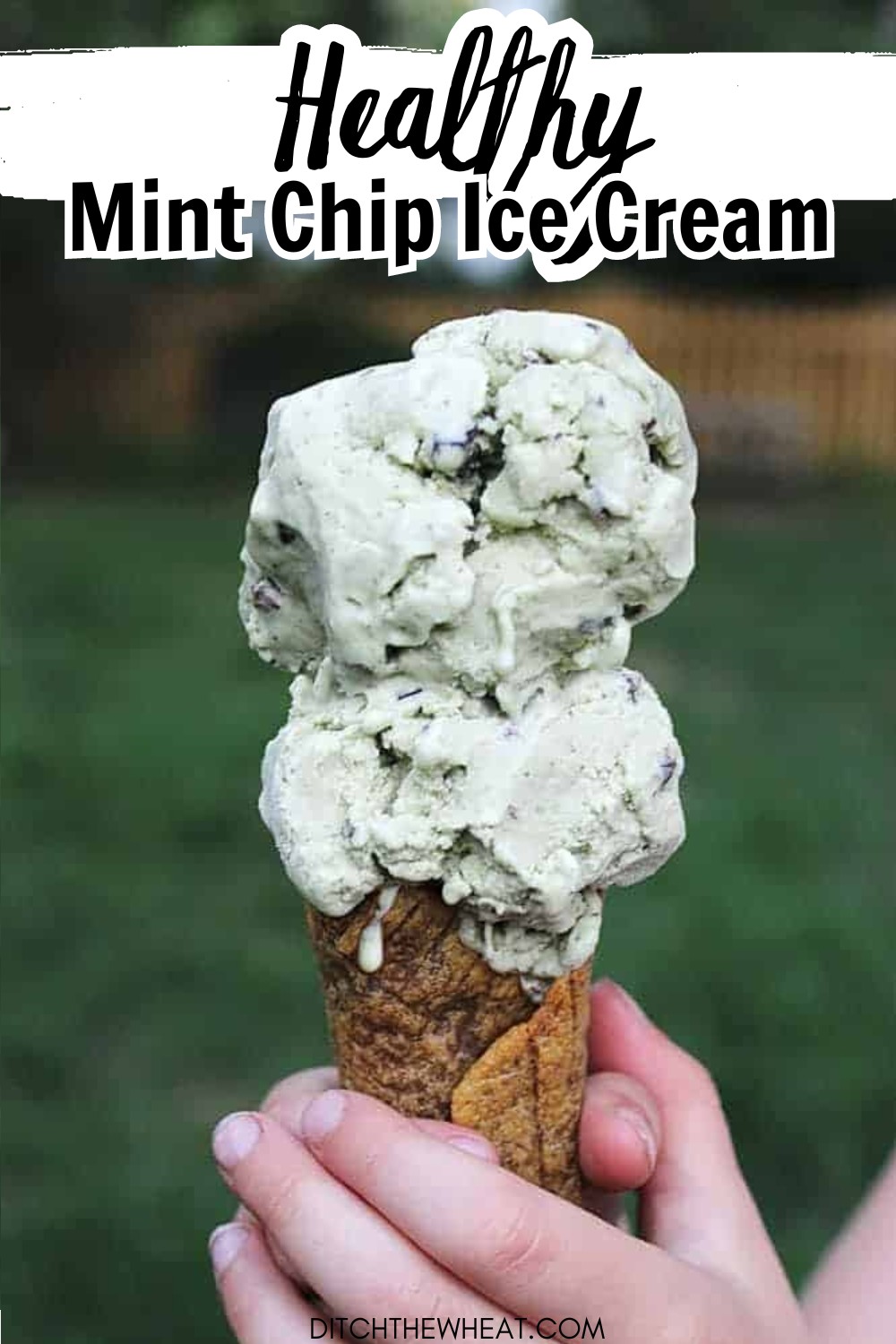 A child's hand is holding an ice cream cone with two scoops of dairy-free mint Chip Ice cream.