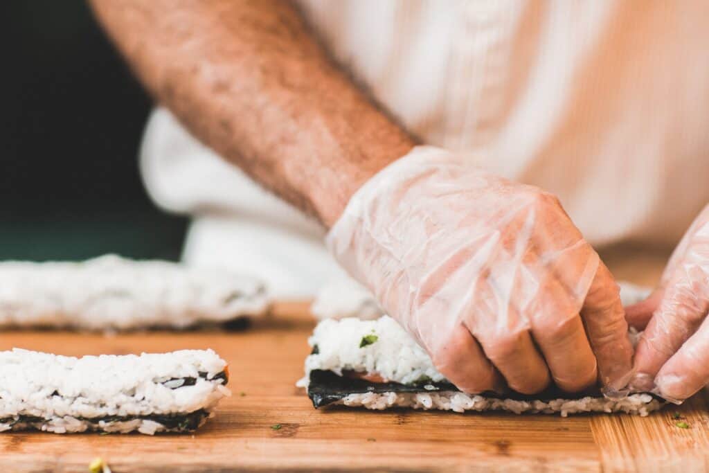 A man's hands preparing a roll of sushi.