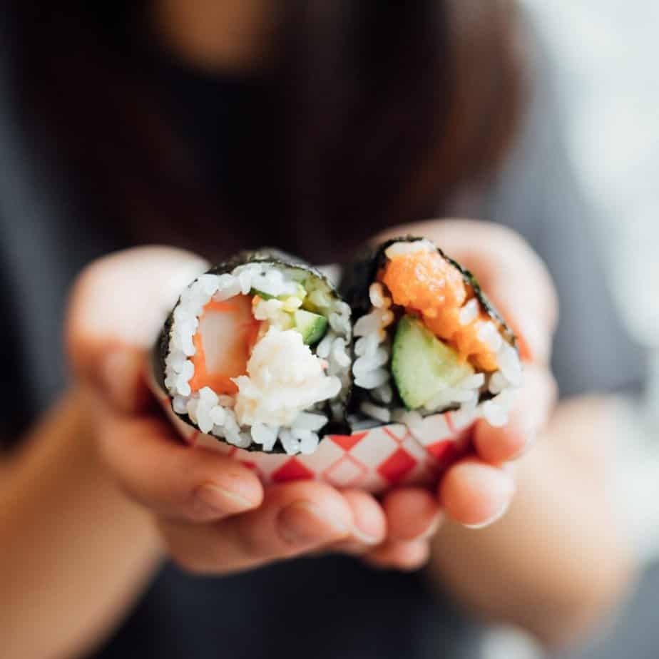 Hands holding two pieces of sushi.