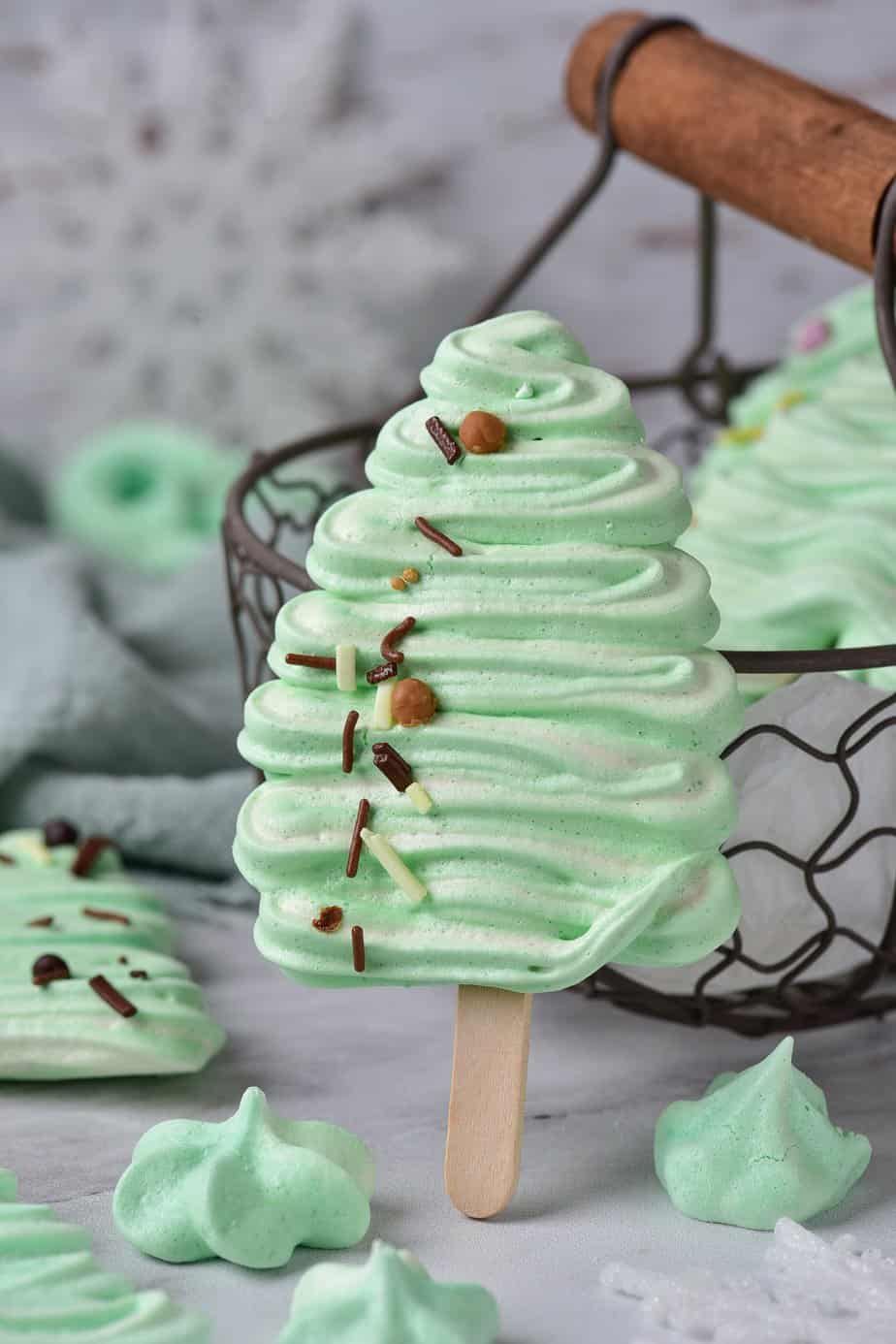 Meringue Christmas Trees on a stick leaning against a basket.