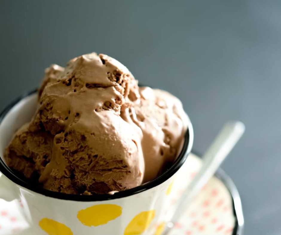 A cup with scoops of dairy-free chocolate ice cream and a plate with a spoon.