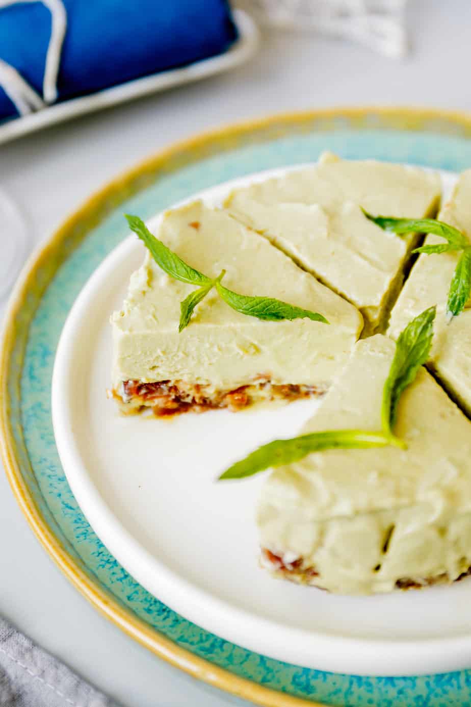 A plate with sliced avocado cheesecake that is garnished with fresh mint.