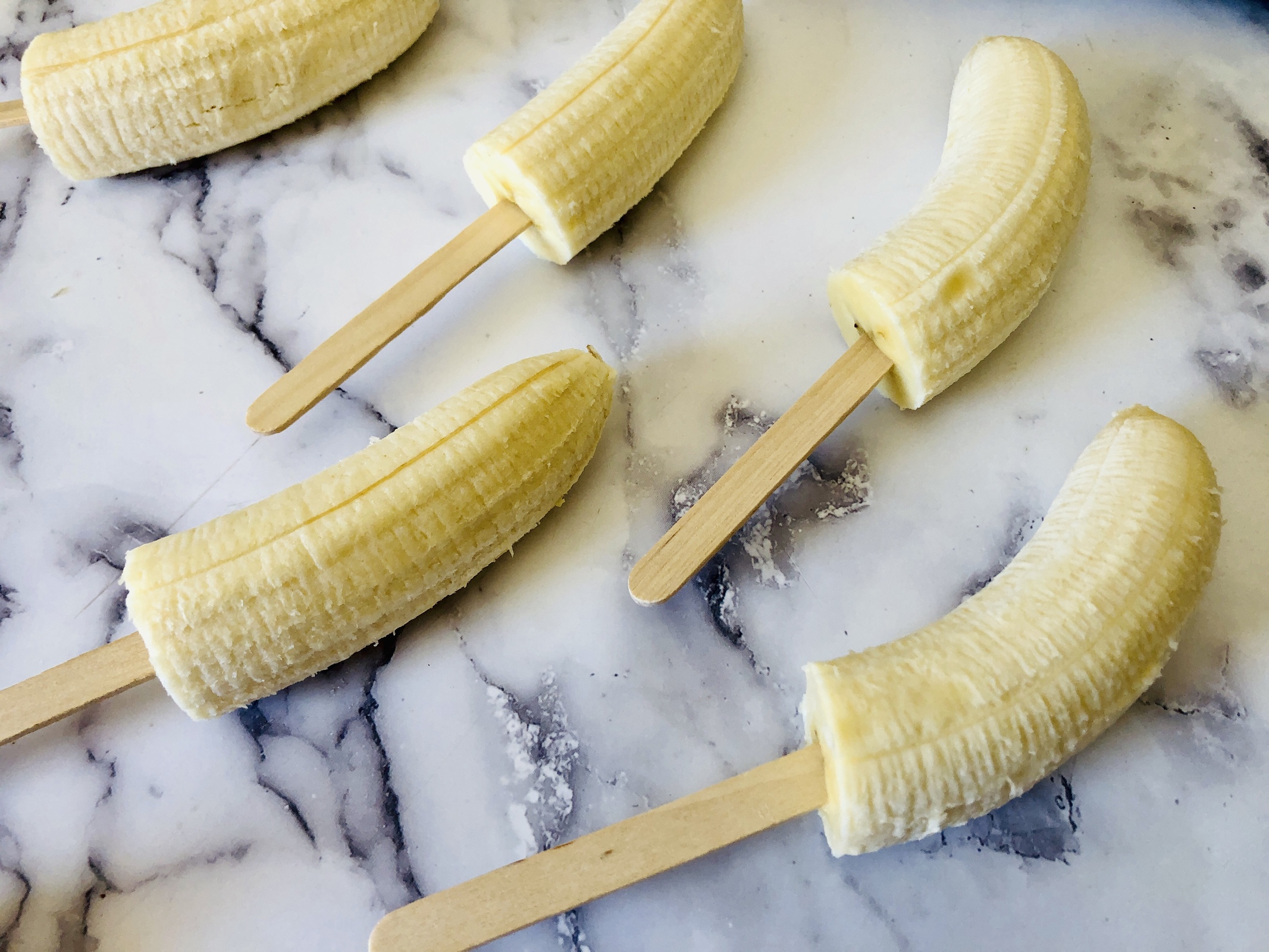 Preparing to make frozen yogurt banana pops. Bananas with popsicle sticks in them. 