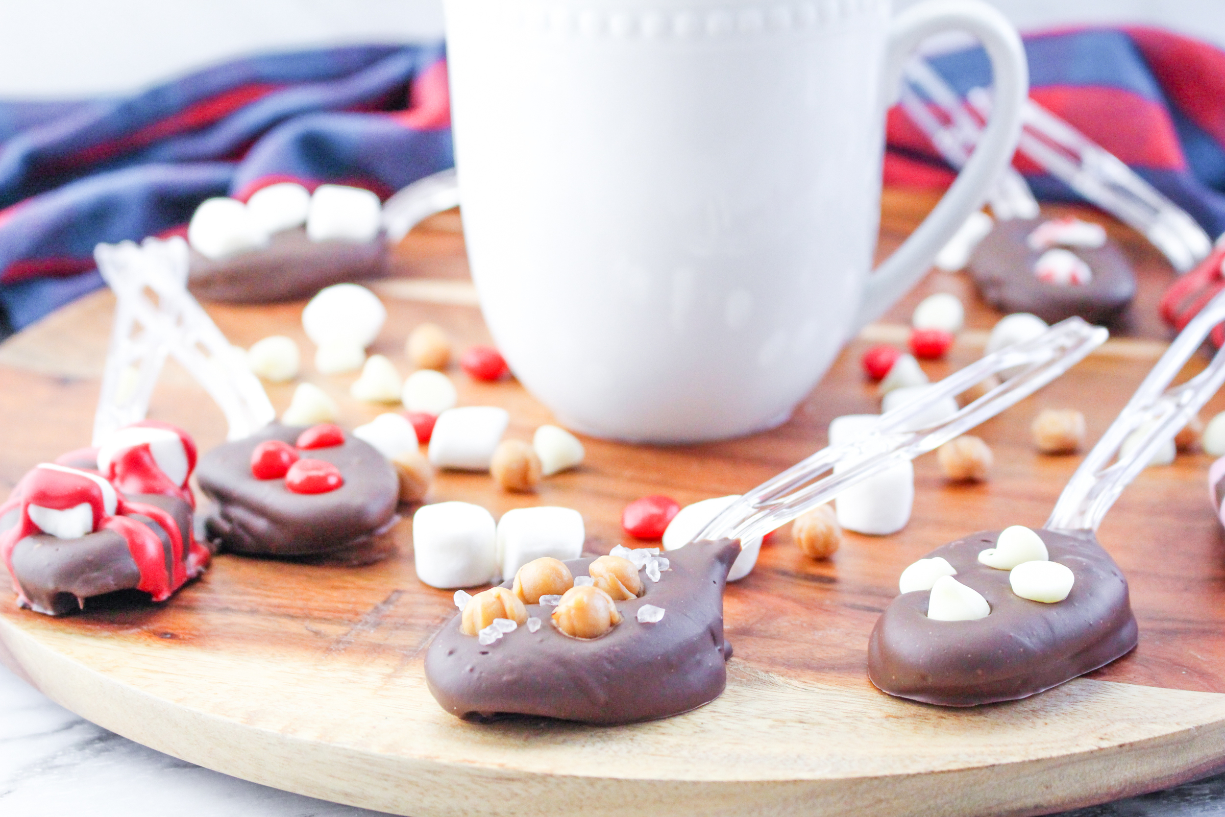 A white mug with hot chocolate and various diy hot chocolate spoons on a wooden background.