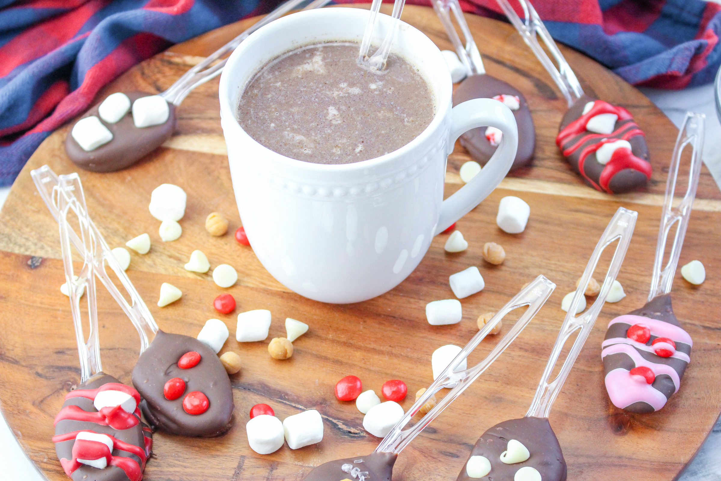A white mug with hot chocolate and various diy hot chocolate spoons on a wooden background.