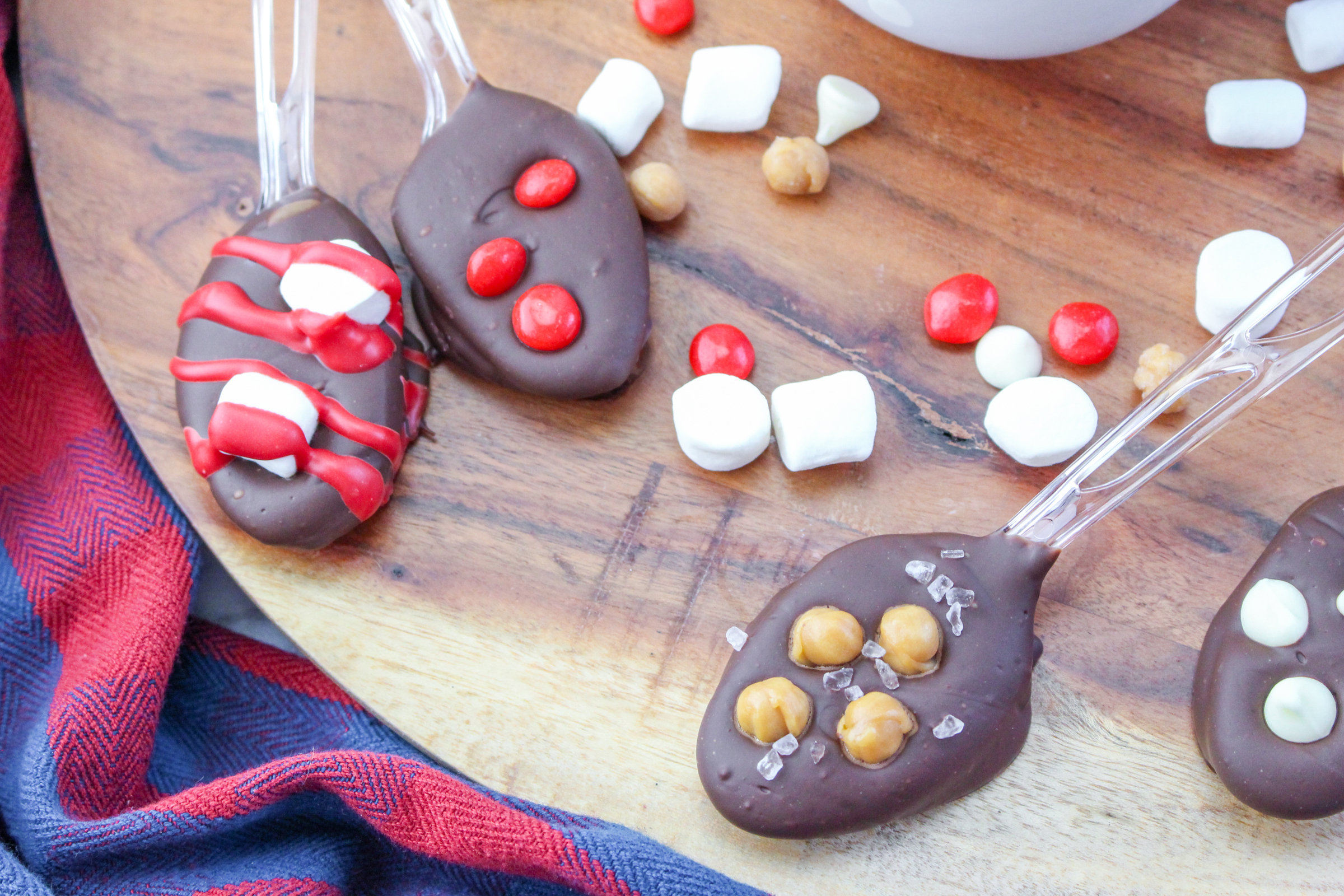 Four hot chocolate spoons on a wooden background with a red and blue cloth.