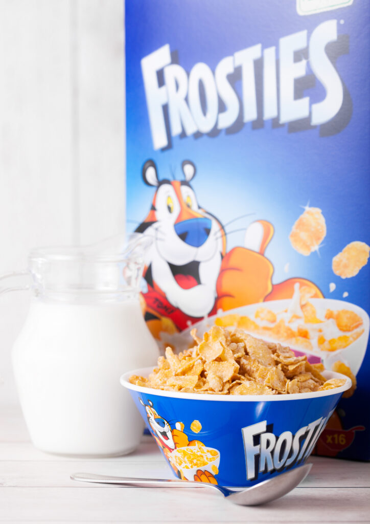 Are Frosted Flakes Gluten Free? A bowl of Frosted Flakes and the box of cereal with a jar of milk. 