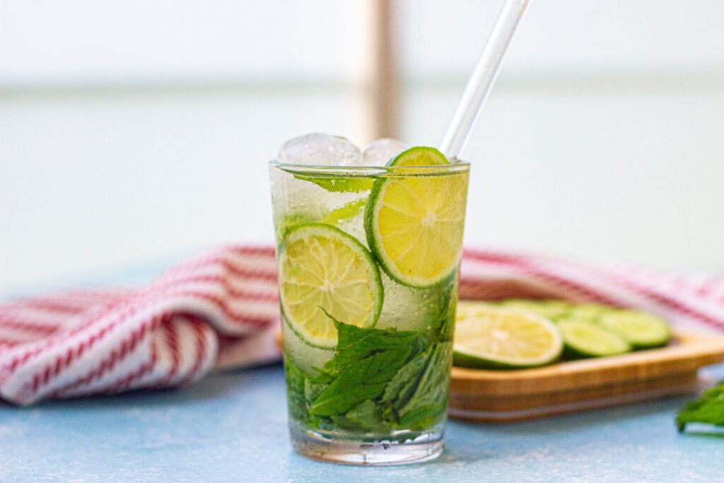 Lime and cucumber water in a glass with a straw.