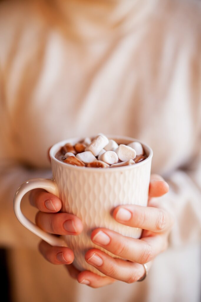 A woman holding a mug of hot chocolate with marshmallows.