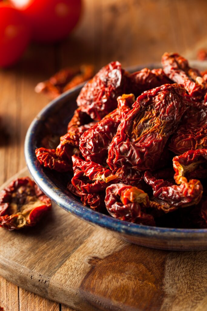 A bowl of sun dried tomatoes on top of a wooden cutting board