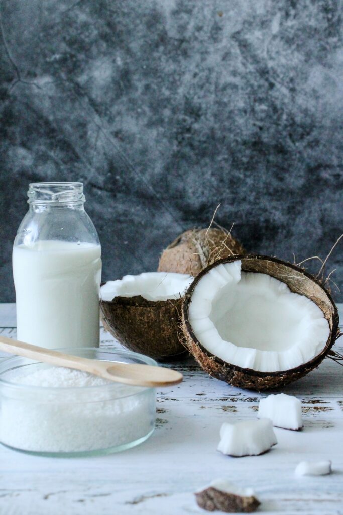A container of coconut milk and a bowl of coconut flakes with a coconut cut in half.