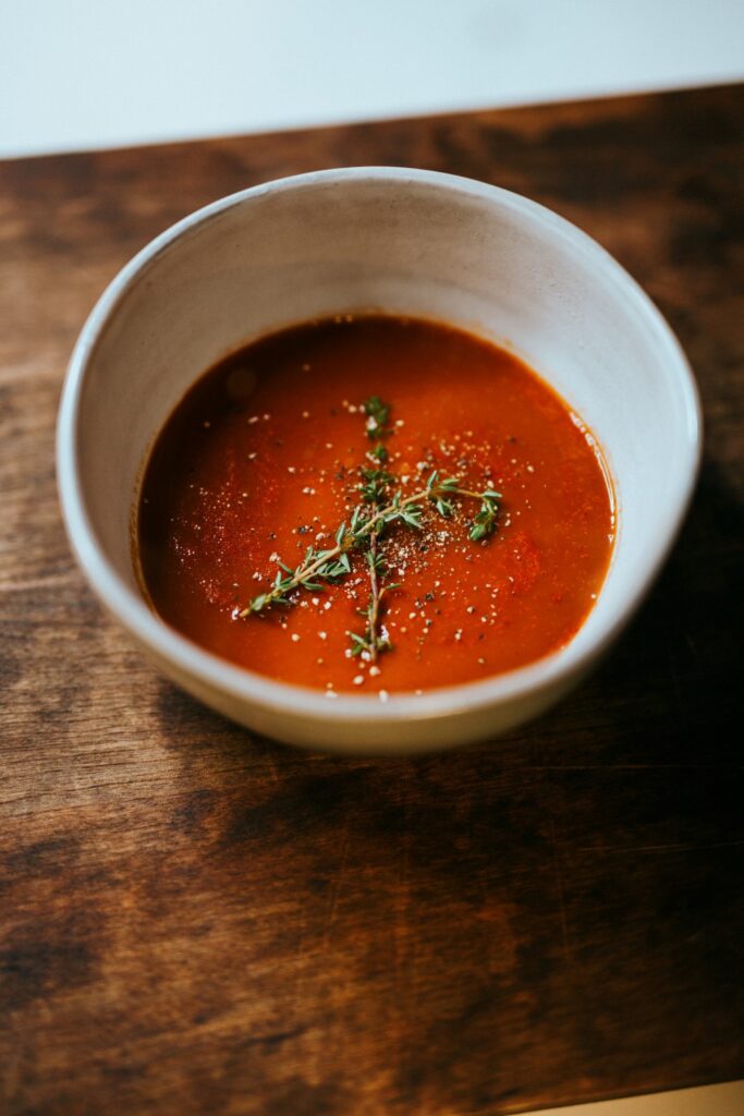 Tomato soup in a white bowl with two sprigs of oregano.