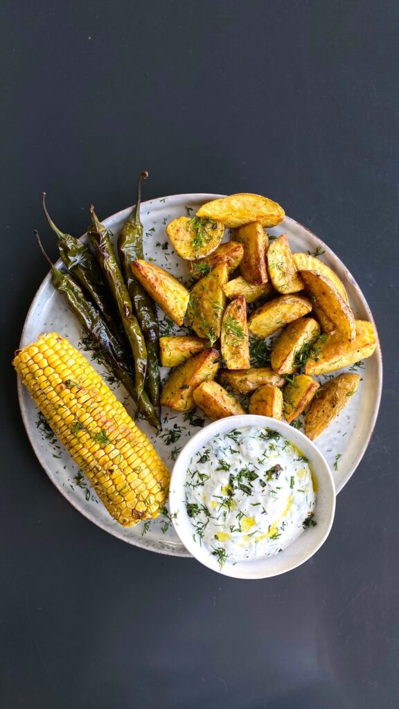 Corn on the cob with potato wedges, grilled peppers, and a dip.