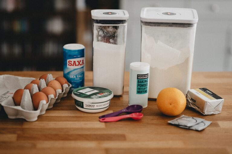 Eggs, baking powder, flour, and other baking ingredients on a wooden background.