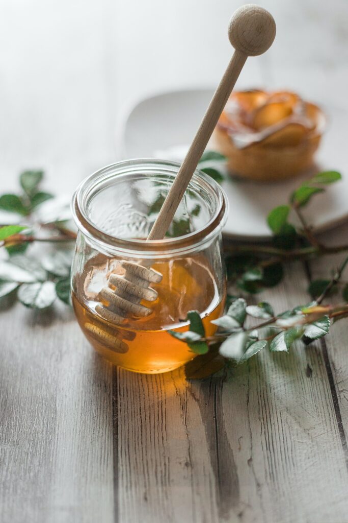 A glass jar of honey with a honey stick.