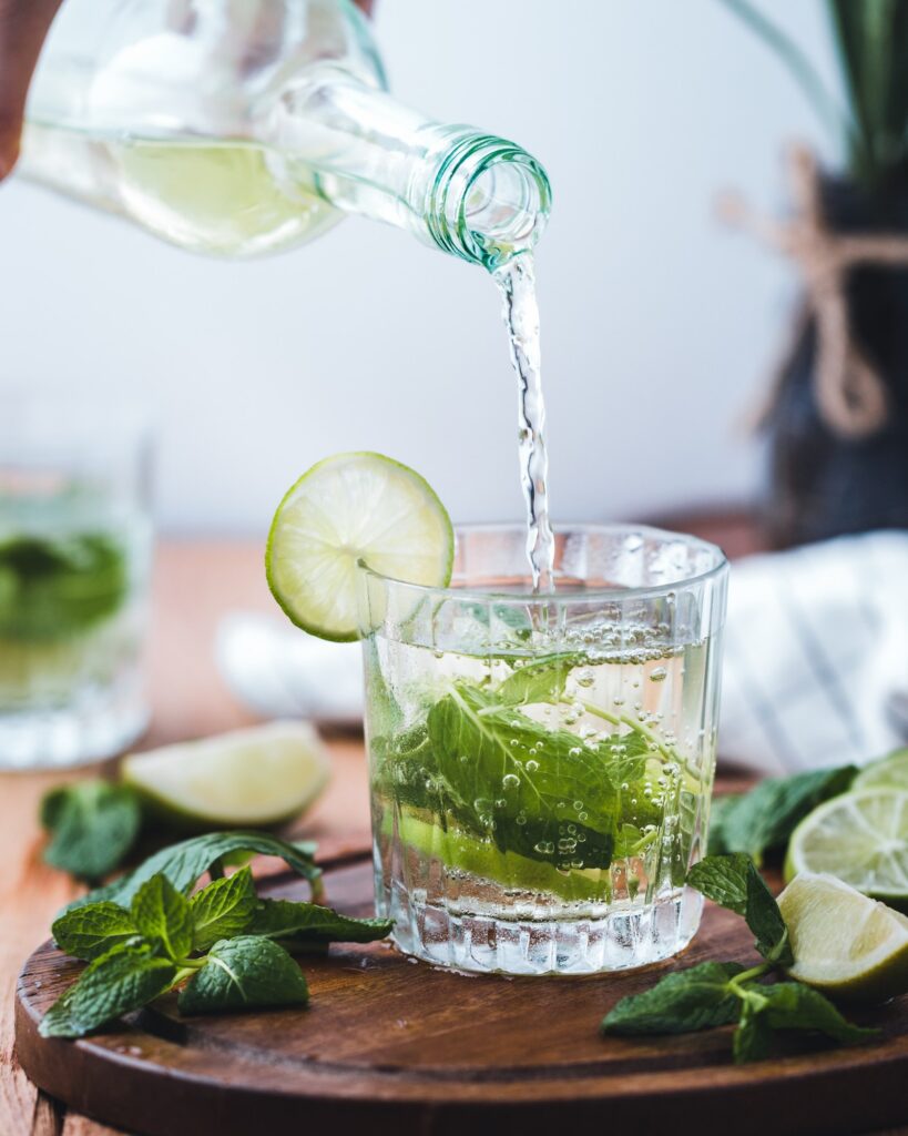 A bottle of rum being poured into a glass with mojito ingredients.