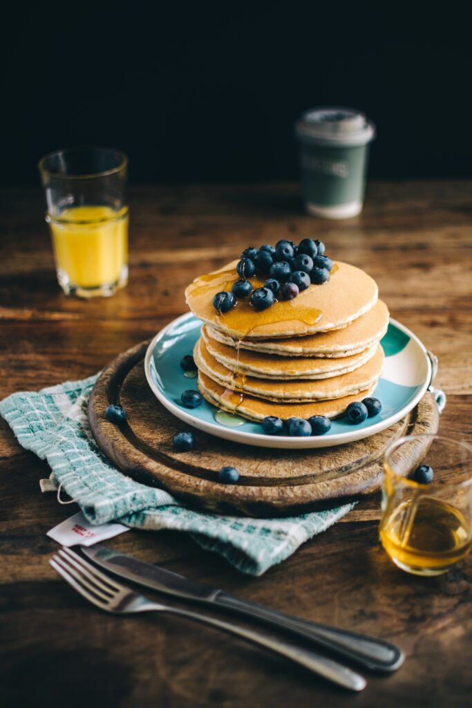 A stack of pancakes with blueberries and a glass of orange juice.