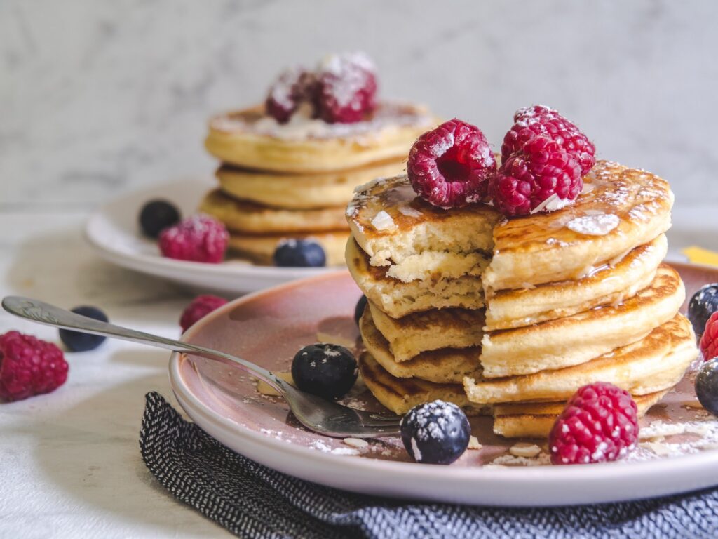 A stack of pancakes with a raspberries and blueberries and it has been cut into to show the fluffy inside.
