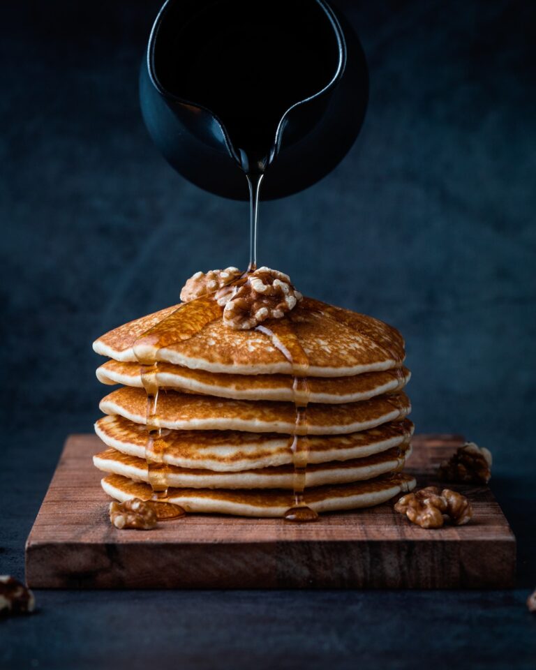 A stack of pancakes with a dark background with maple syrup being poured over it.