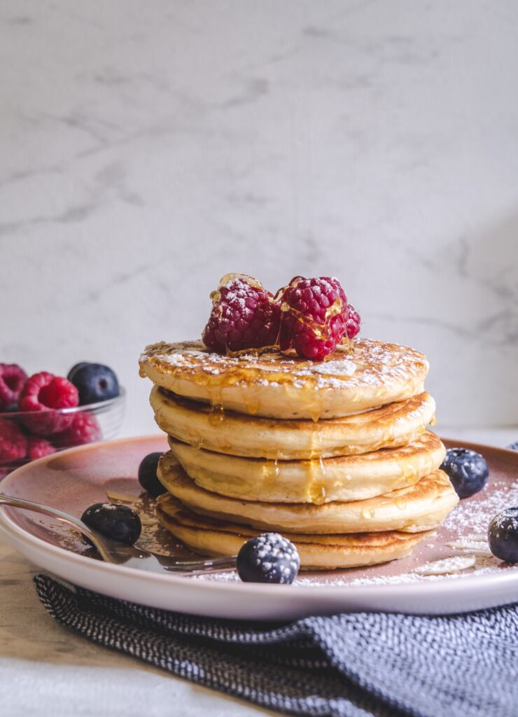 A stack of pancakes with a raspberries and blueberries.