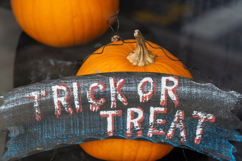 Trick or treat sign Infront of two pumpkins.