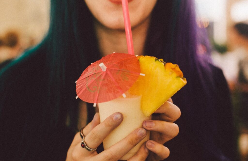 A woman drinking a Pina colada with a mini umbrella and a slice of pineapple.