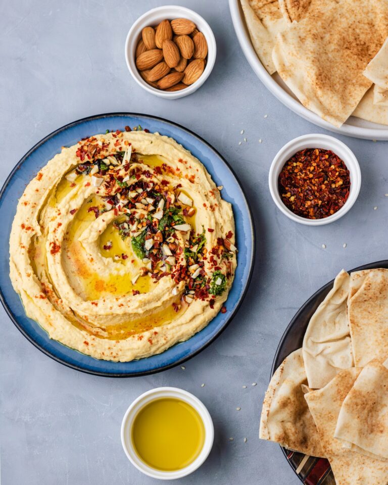 A bowl of hummus with plates of pita bread.