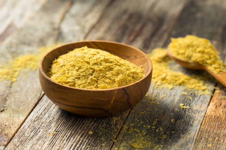 Nutritional Yeast is a wooden bowl with a spoon filled with nutritional yeast.