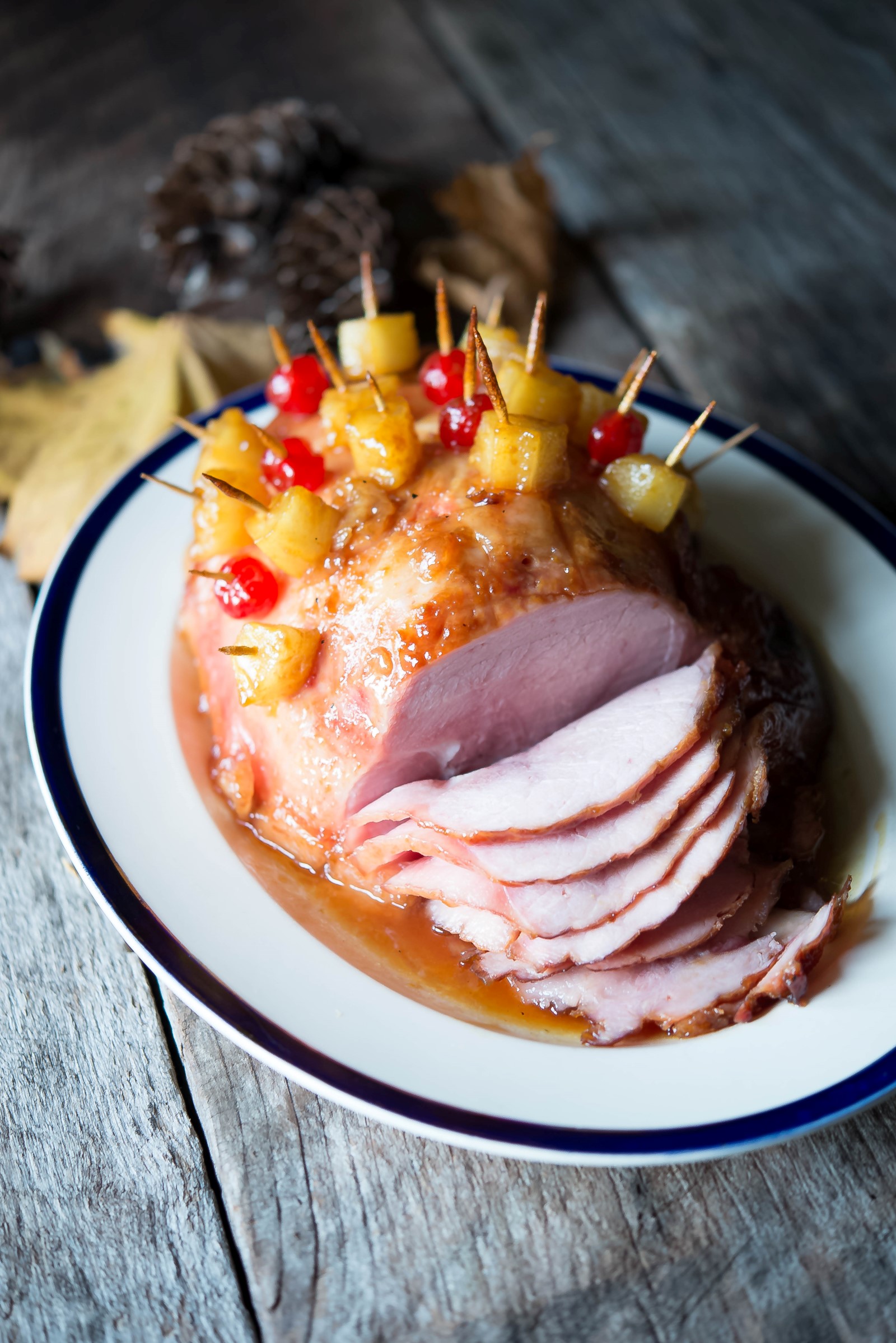 A white platter with a ham that has pineapple and cherries and is sliced. 