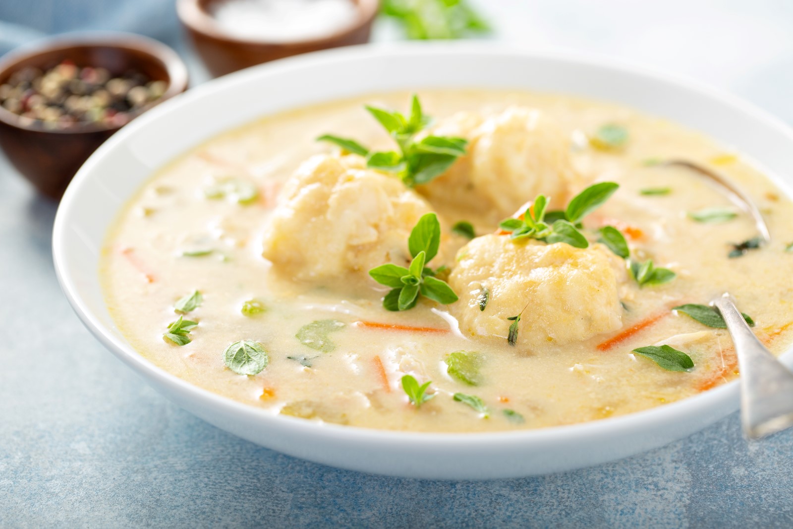 A bowl with chicken and dumplings soup with a spoon.