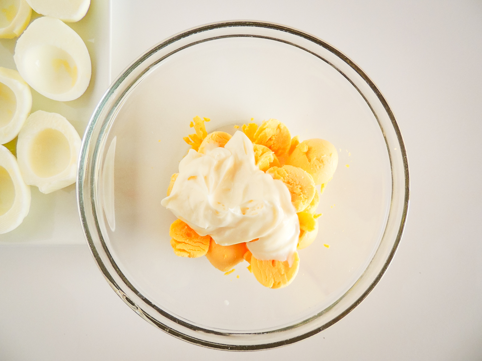 A glass bowl filled with egg yolks and mayonnaise.