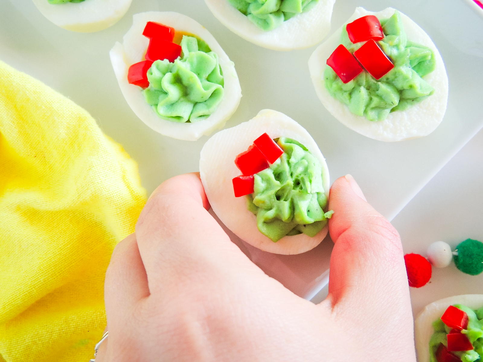 A tray with Christmas deviled eggs and a hand holding one.