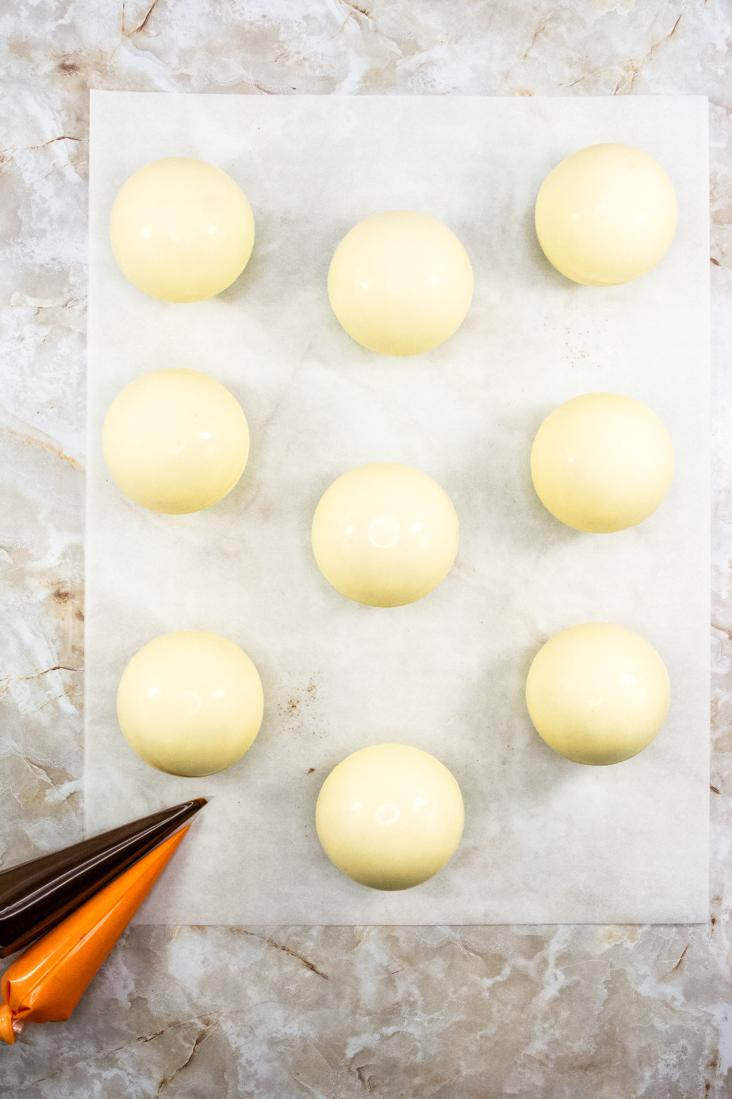 Nine white chocolate cocoa bombs waiting to be decorated on parchment paper.