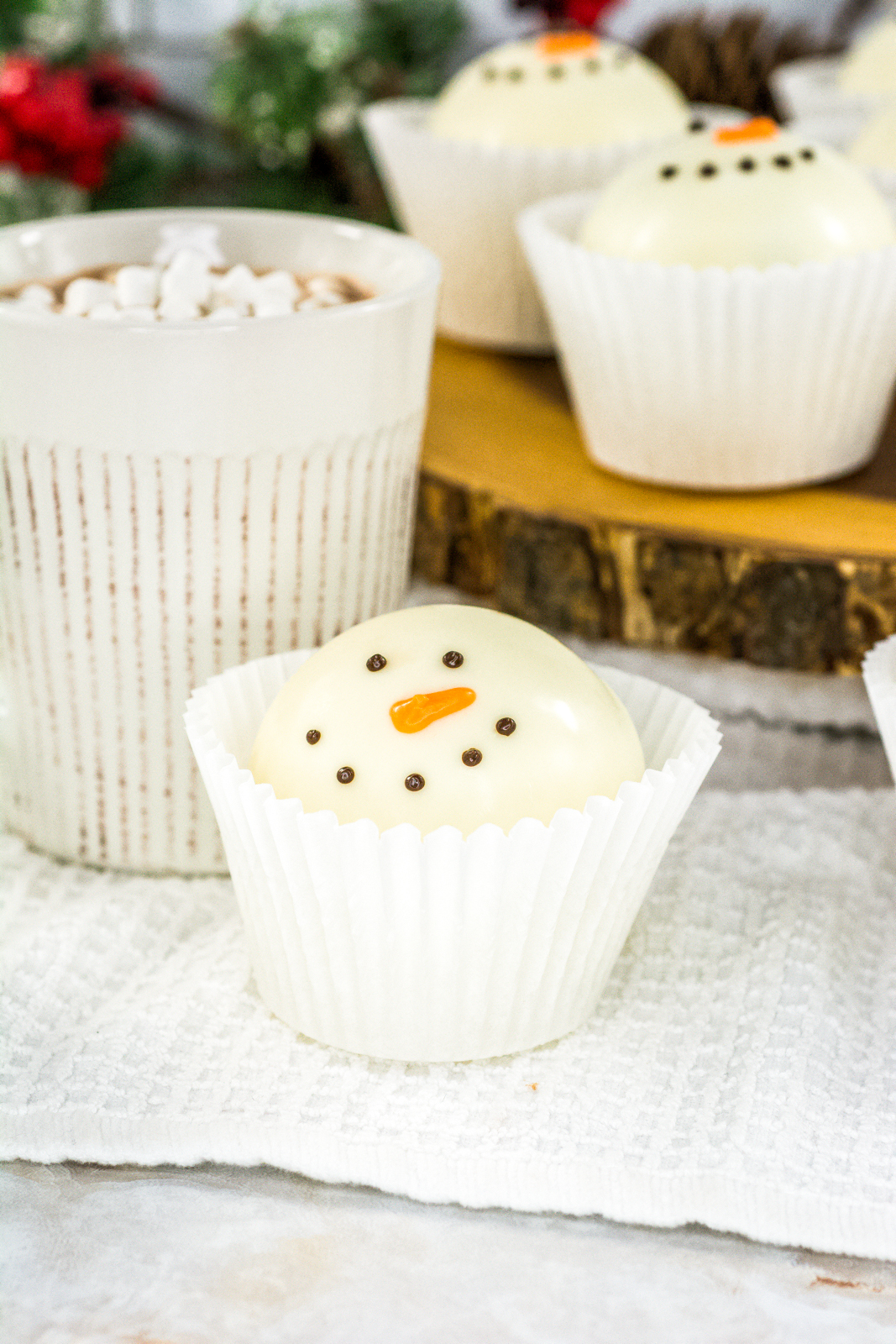 A white mug with a melting snowman hot chocolate bomb with more bombs around it.