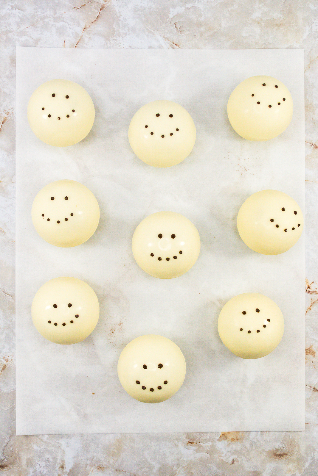Nine white chocolate cocoa bombs decorated with eyes and a smile. 