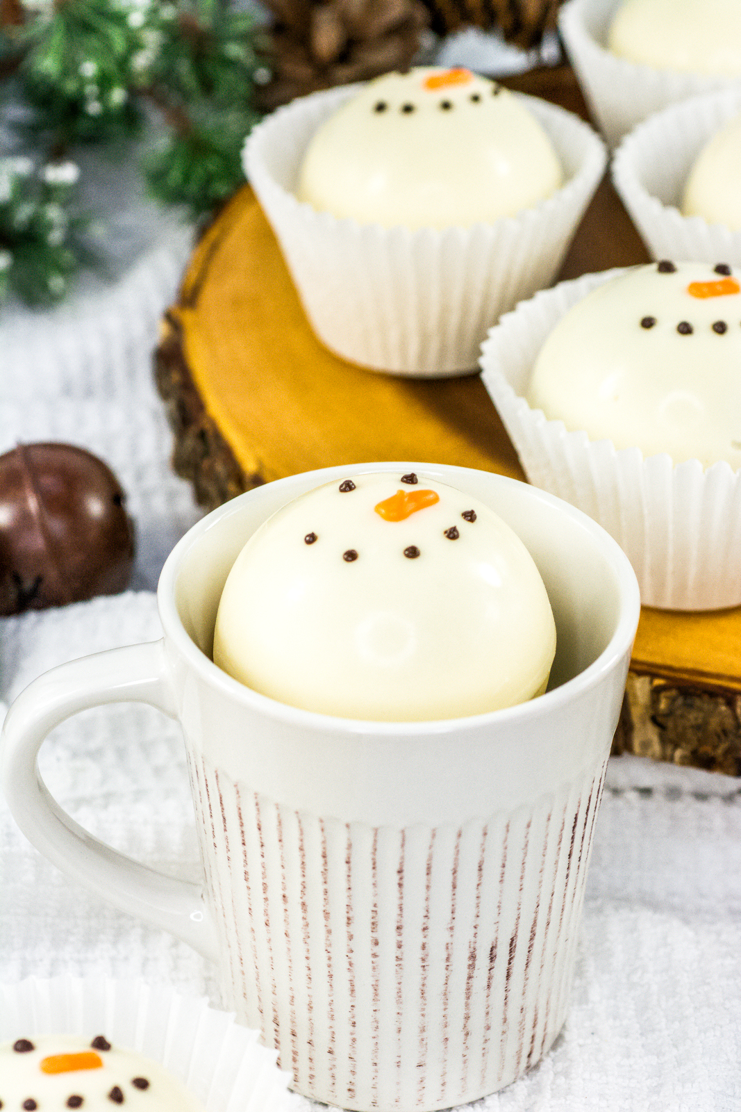 A white mug with a melting snowman hot chocolate bomb with more bombs around it.