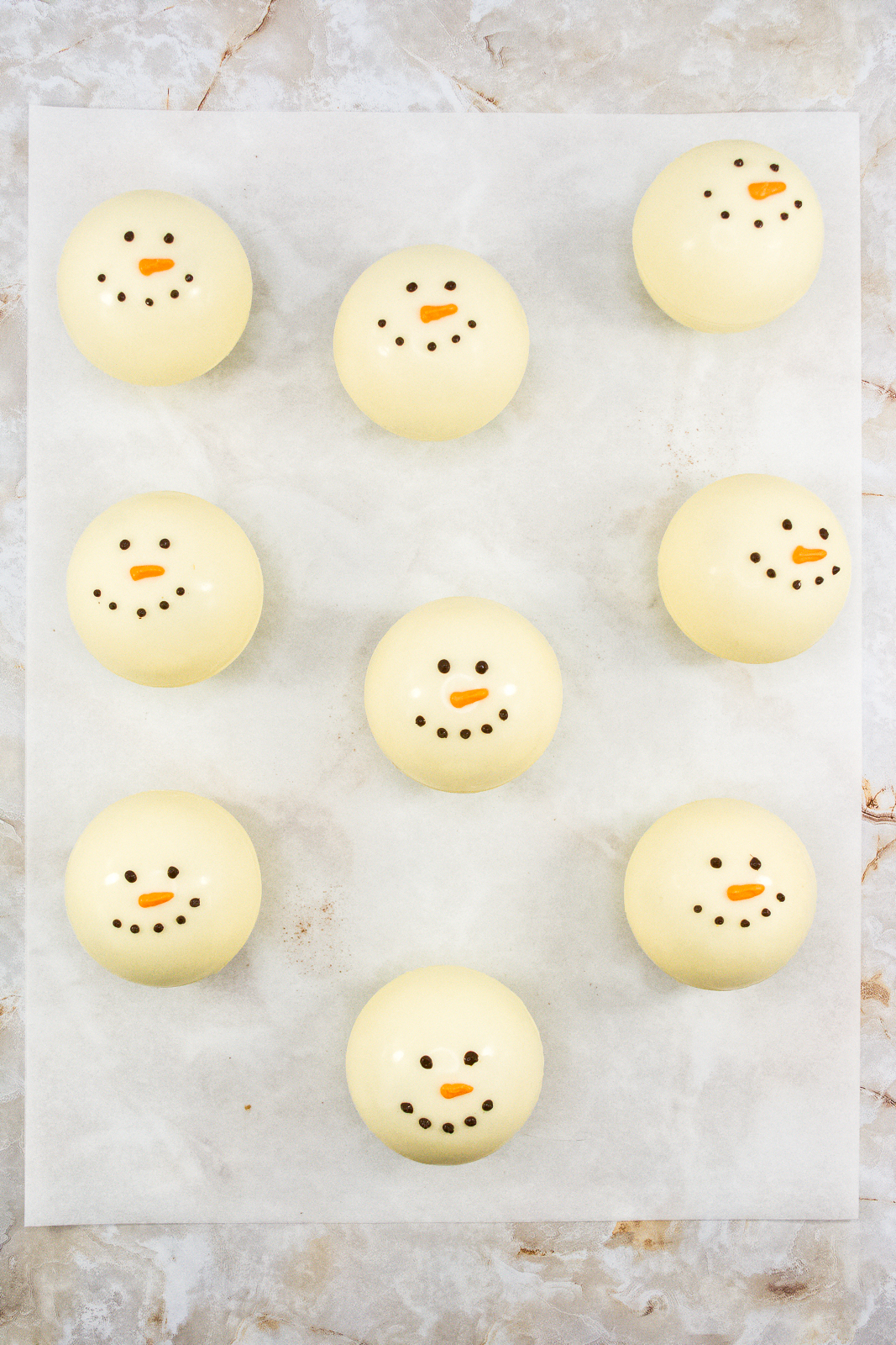Nine white chocolate cocoa bombs decorated with eyes and a smile.