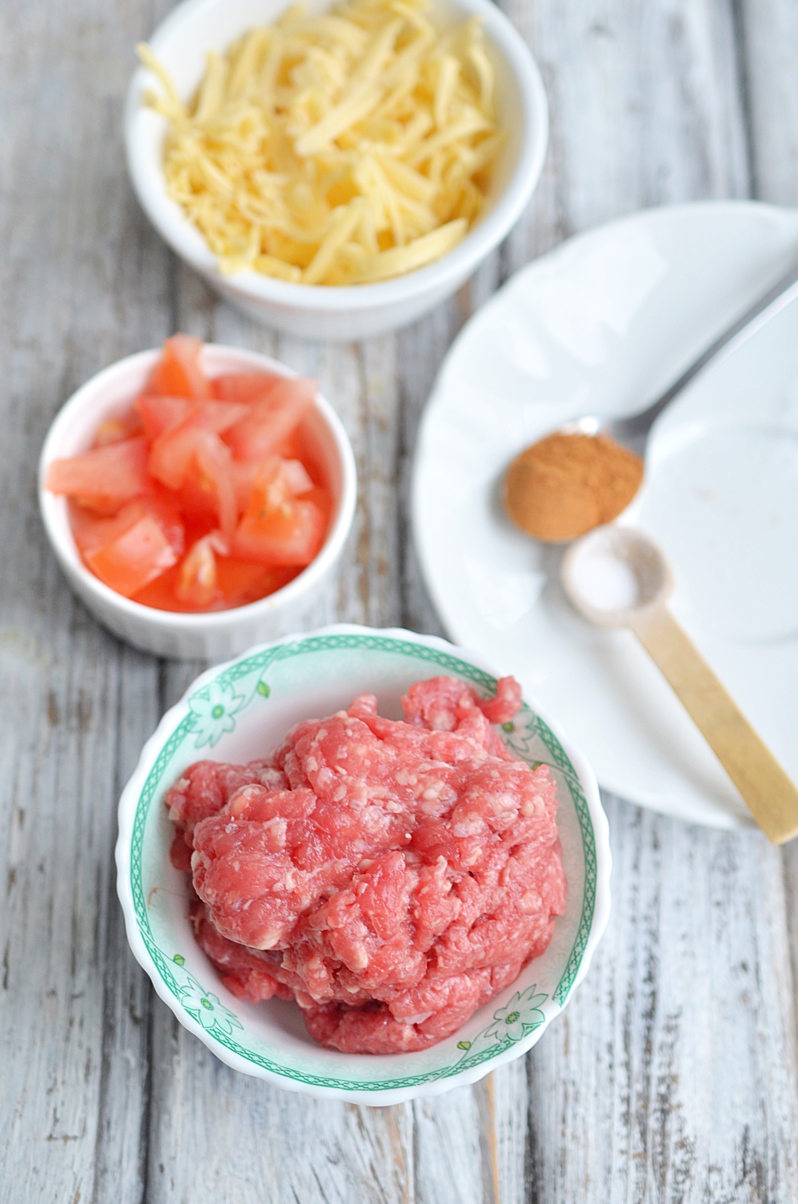 A bowl of shredded cheese, tomatoes, and raw ground beef.