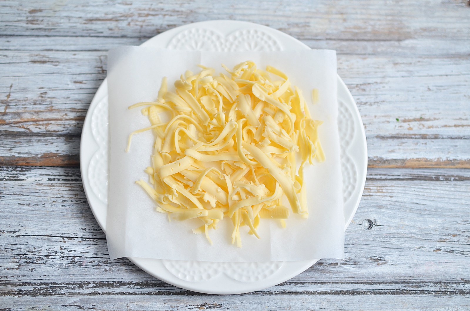 A white plate with a sheet of parchment paper and shredded cheese formed in a circle.