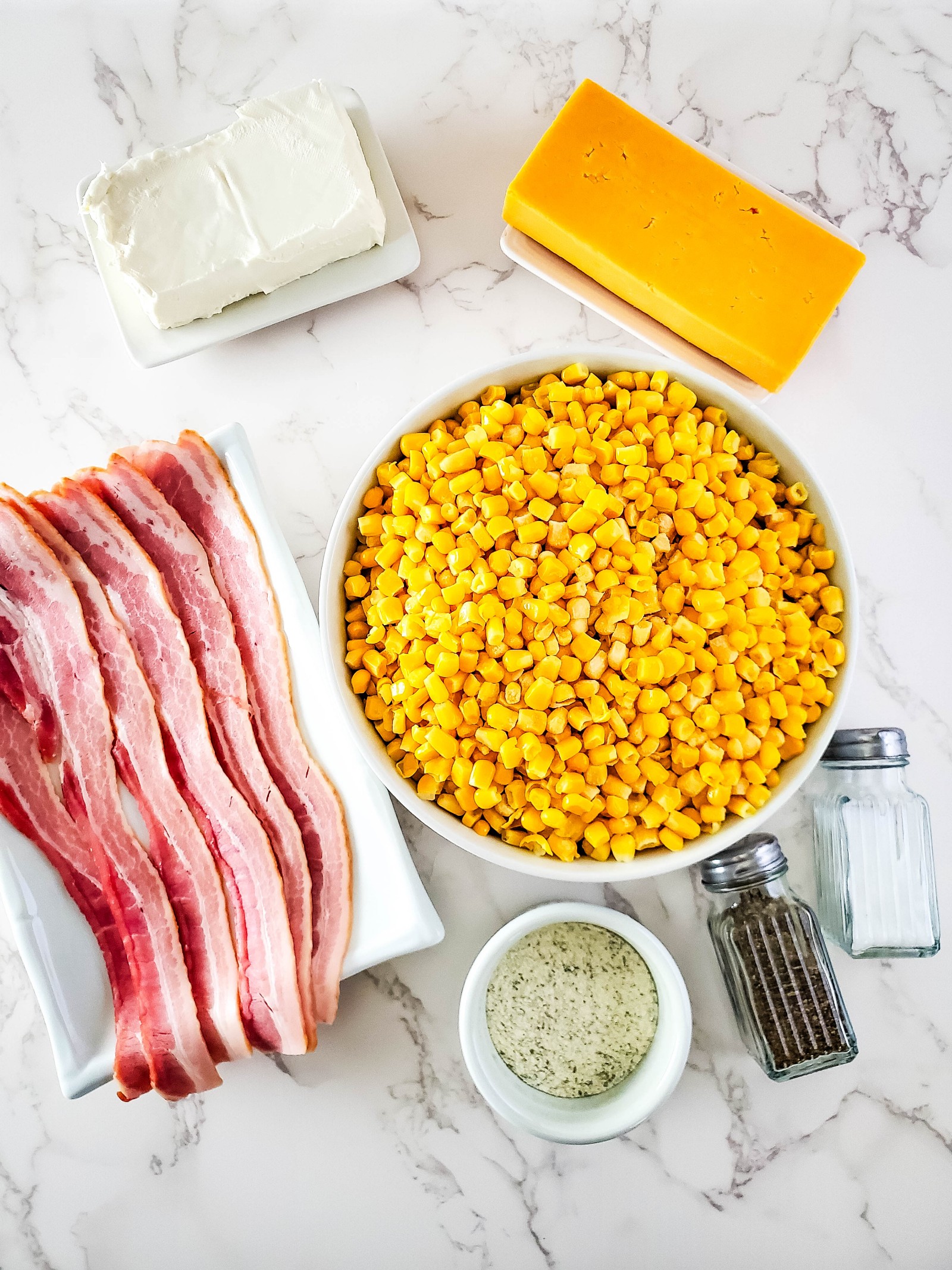 The ingredients for Crockpot corn with cream cheese. Bacon, cream cheese, frozen corn, ranch seasoning, and cheddar cheese.