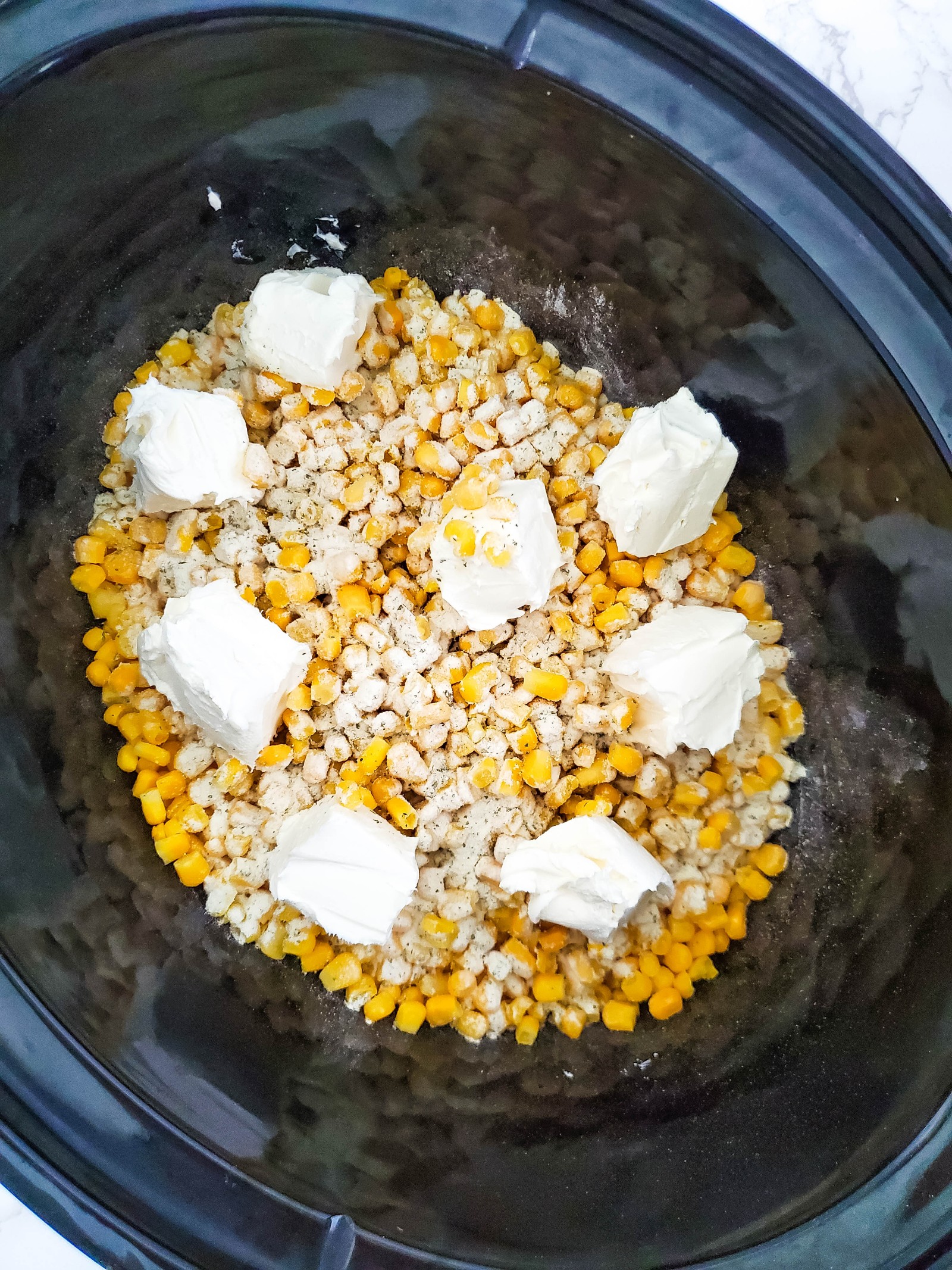 Cubes of cream cheese added to a Crockpot with frozen corn.
