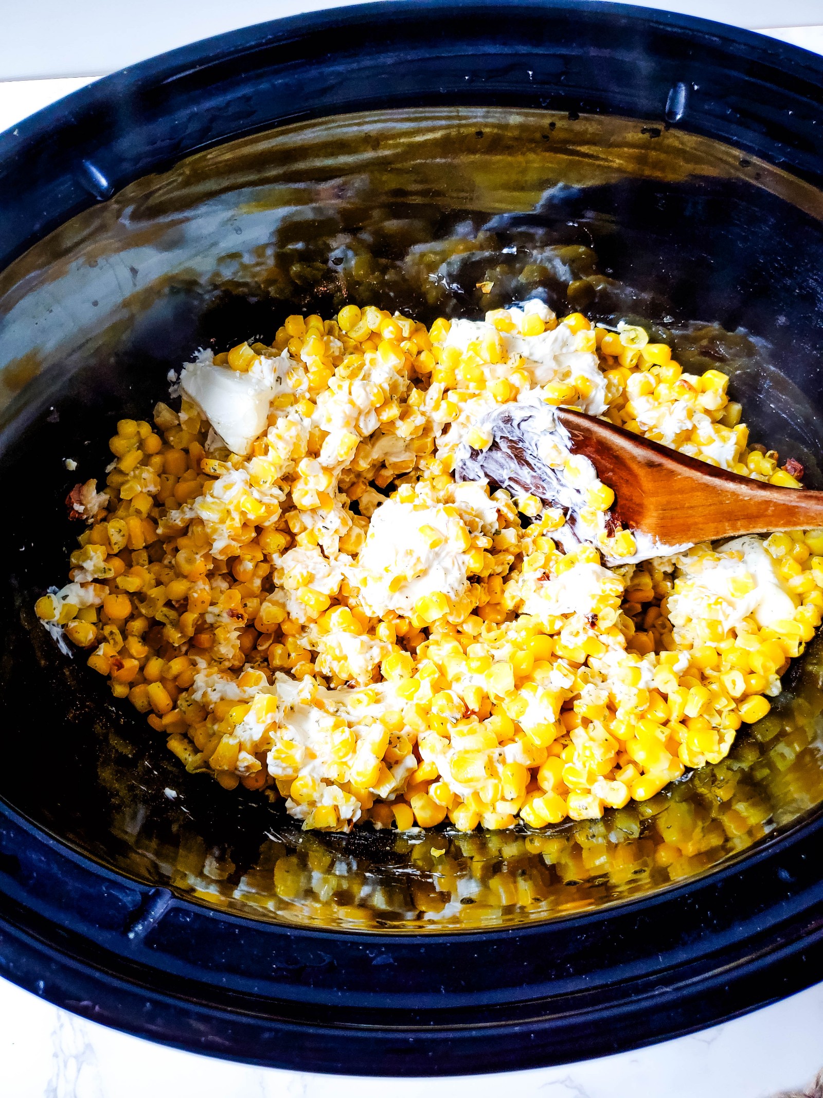 A wooden spoon stirring the cream cheese corn casserole.